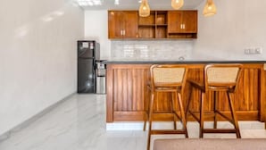 A modern kitchen with wooden cabinets, a black refrigerator, and two wicker chairs. - The Umah Pandawa 2 (Bali)