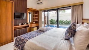A hotel room with a bed, a TV, a sliding door to a balcony, and a wooden panel wall. - The Umah Pandawa 2 (Bali)