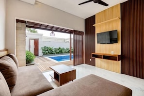 A modern living room with a sofa, a coffee table, and a TV mounted on a wooden wall. - The Umah Pandawa 2 (Bali)