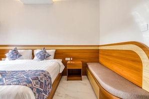 A hotel room with a wooden headboard, a bed with a patterned bedspread, a bedside table, and a bench. - The Umah Pandawa 2 (Bali)