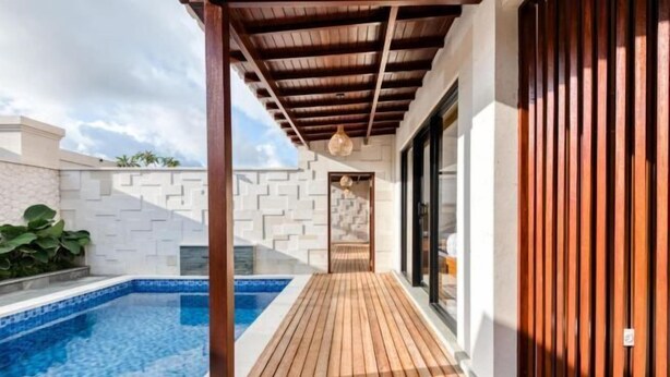 A wooden deck leading to a swimming pool with a clear blue water feature, a white brick wall, and a wooden fence. - The Umah Pandawa 2 (Bali)