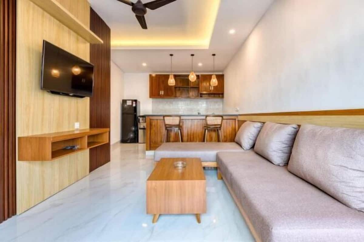 A modern living room with a sofa, coffee table, TV, and wooden shelving.