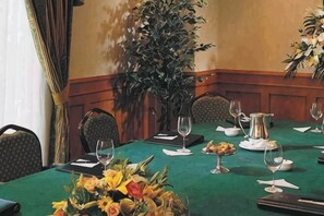 A conference table with chairs, a vase of flowers, a pitcher, and wine glasses.