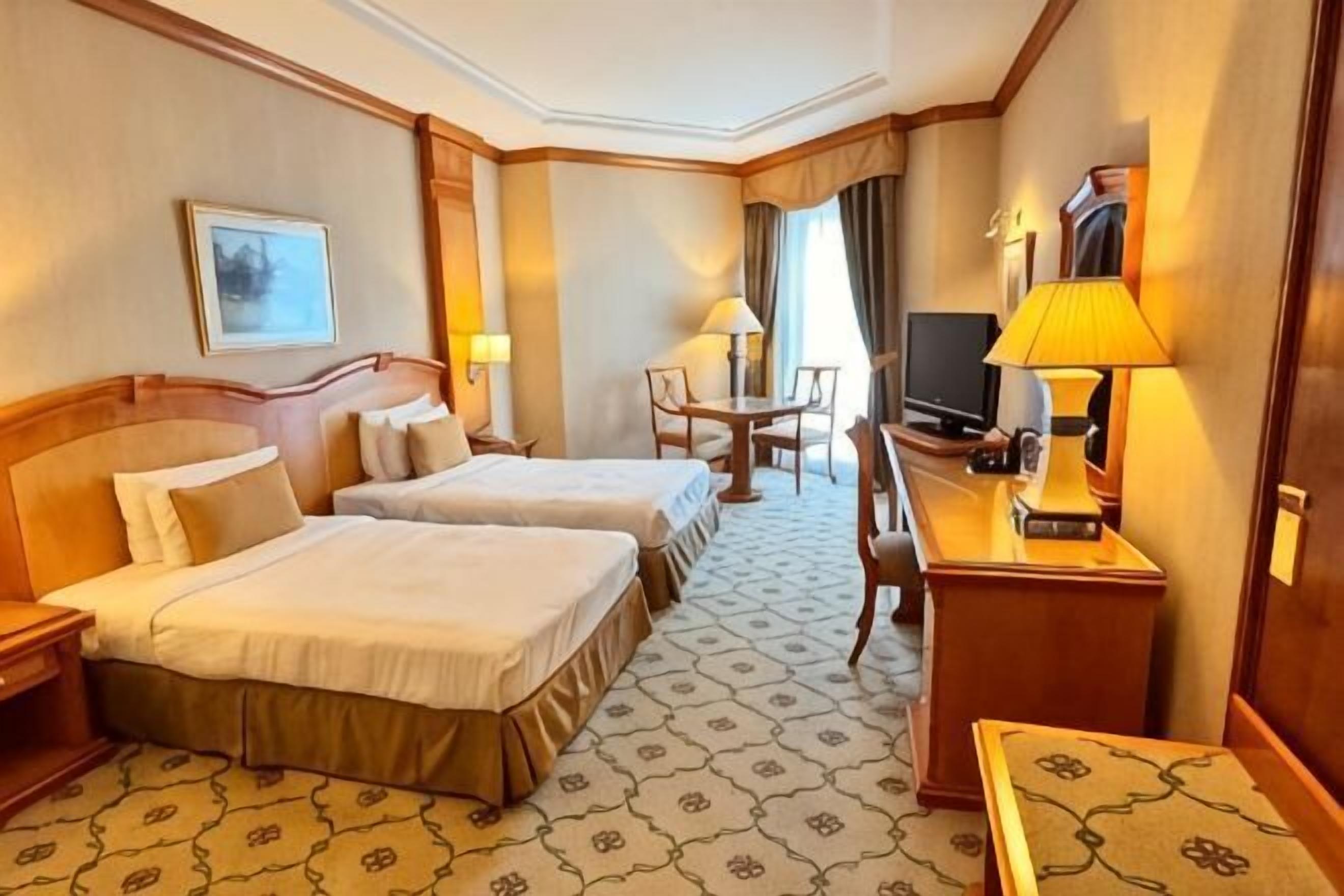 Une chambre d’hôtel avec deux lits, un bureau avec une lampe, une télévision et une chaise.
