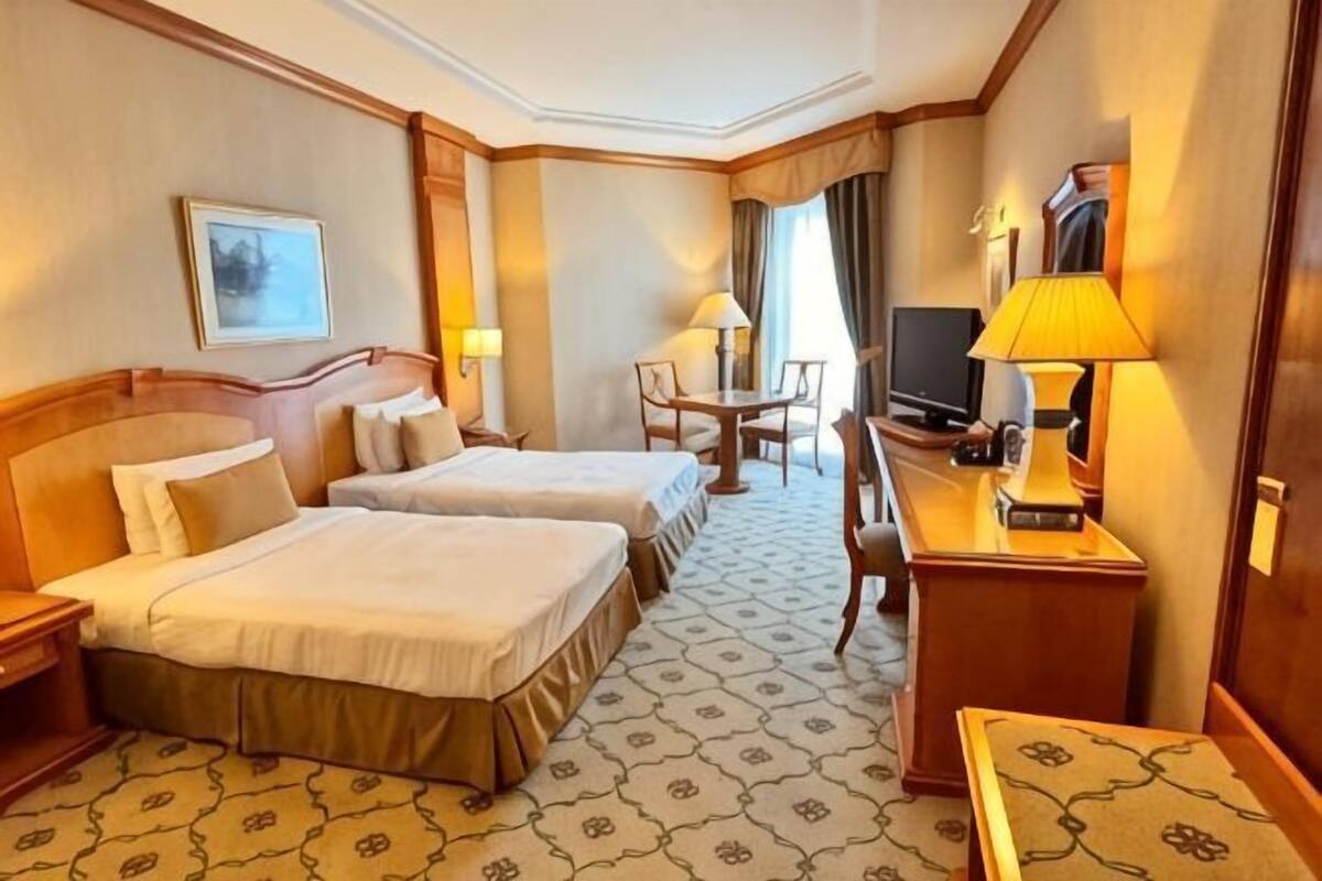 A hotel room with two beds, a desk with a lamp, a television, and a chair.