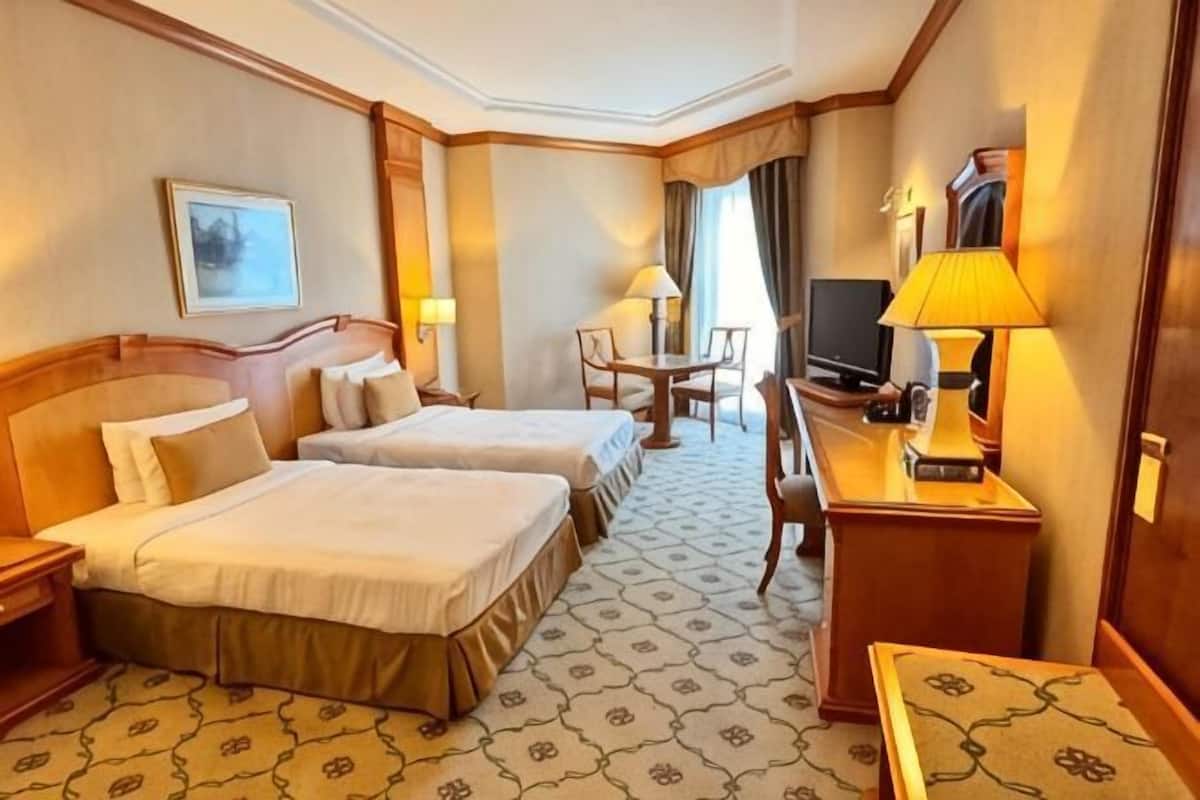 A hotel room with two beds, a desk with a lamp, a television, and a chair.