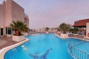 Ein Pool mit Liegestühlen und Palmen, umgeben von Gebäuden.