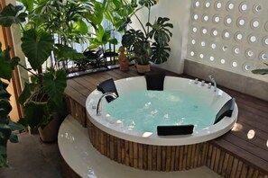 A hot tub with a wooden deck, surrounded by potted plants and a wall with circular cutouts. - GomiHouse-Cozy-4BRs-5 'to Lotte Mart- jacuzzi pool (Da Nang)