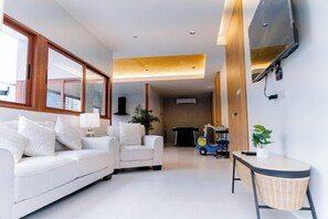A modern living room with a white sofa, a small armchair, a television mounted on the wall, and a toy car. - Holmestay Hatyai (Hat Yai)