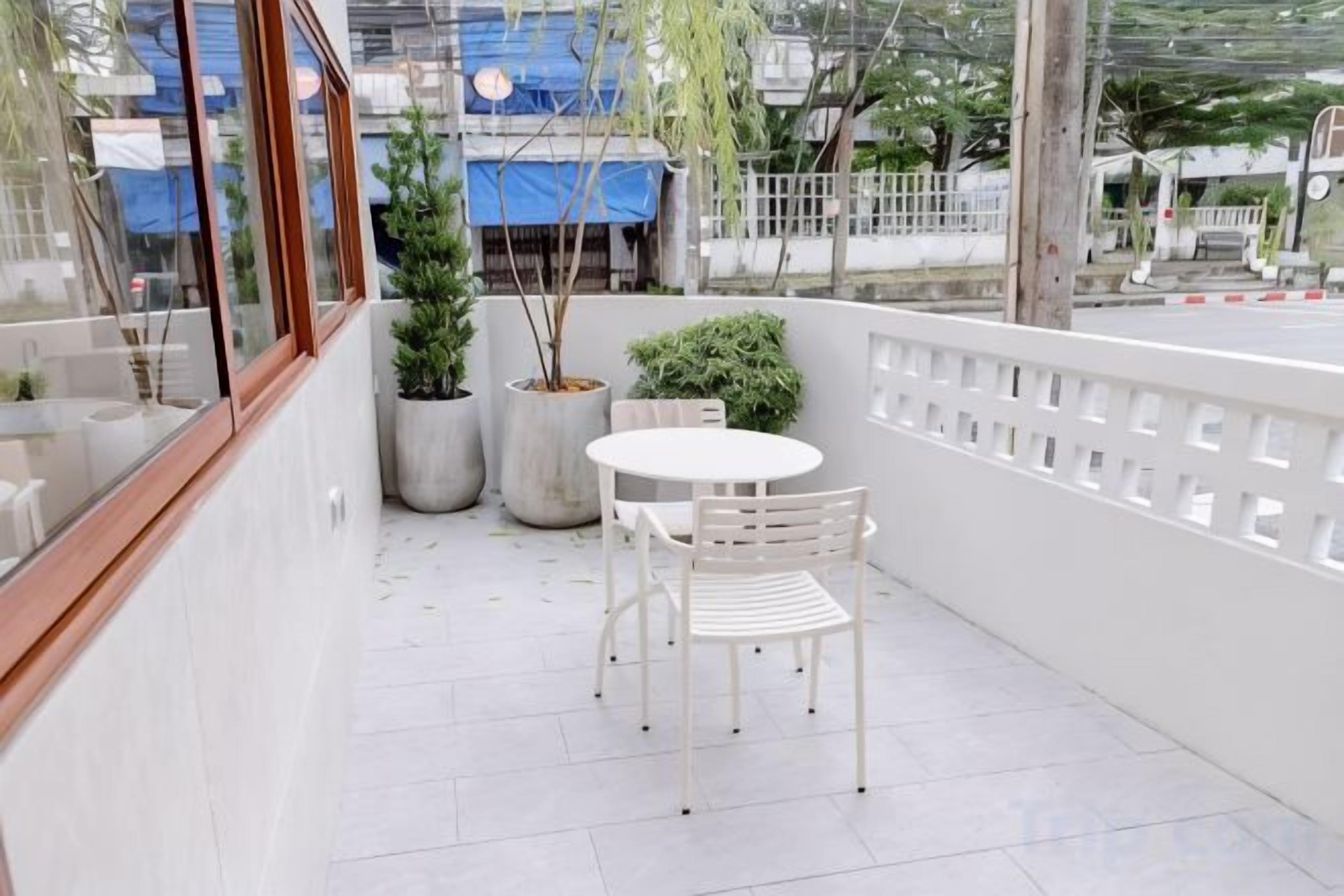 A balcony with a white table and chairs, potted plants, and a view of the street.