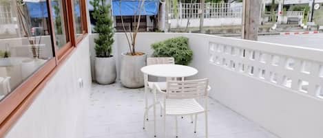A balcony with a white table and chairs, potted plants, and a view of the street.