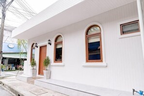 Un bâtiment blanc doté d’un porche, de fenêtres en arc de cercle et d’une porte.
