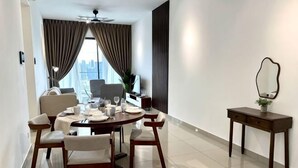A modern dining area with a round table, six chairs, a small side table with a mirror, and a view of the city through large windows. - 2&3BR Family Suite Nr Sunway Velocity & LRT Maluri (Kuala Lumpur)