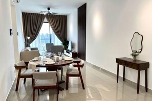 A modern dining area with a round table, six chairs, a small side table with a mirror, and a view of the city through large windows. - 2&3BR Family Suite Nr Sunway Velocity & LRT Maluri (Kuala Lumpur)