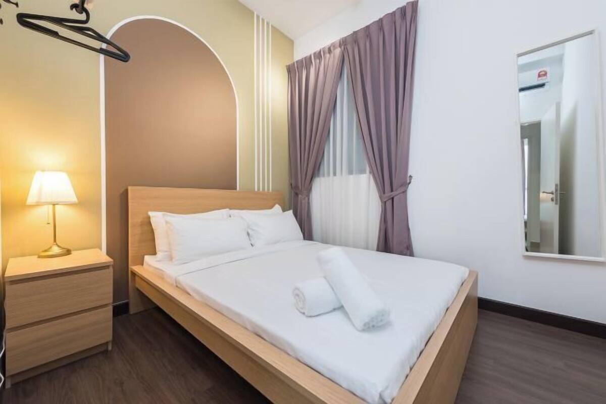 A single bed with white bedding, a bedside lamp, a wooden nightstand, and a mirror on the wall.