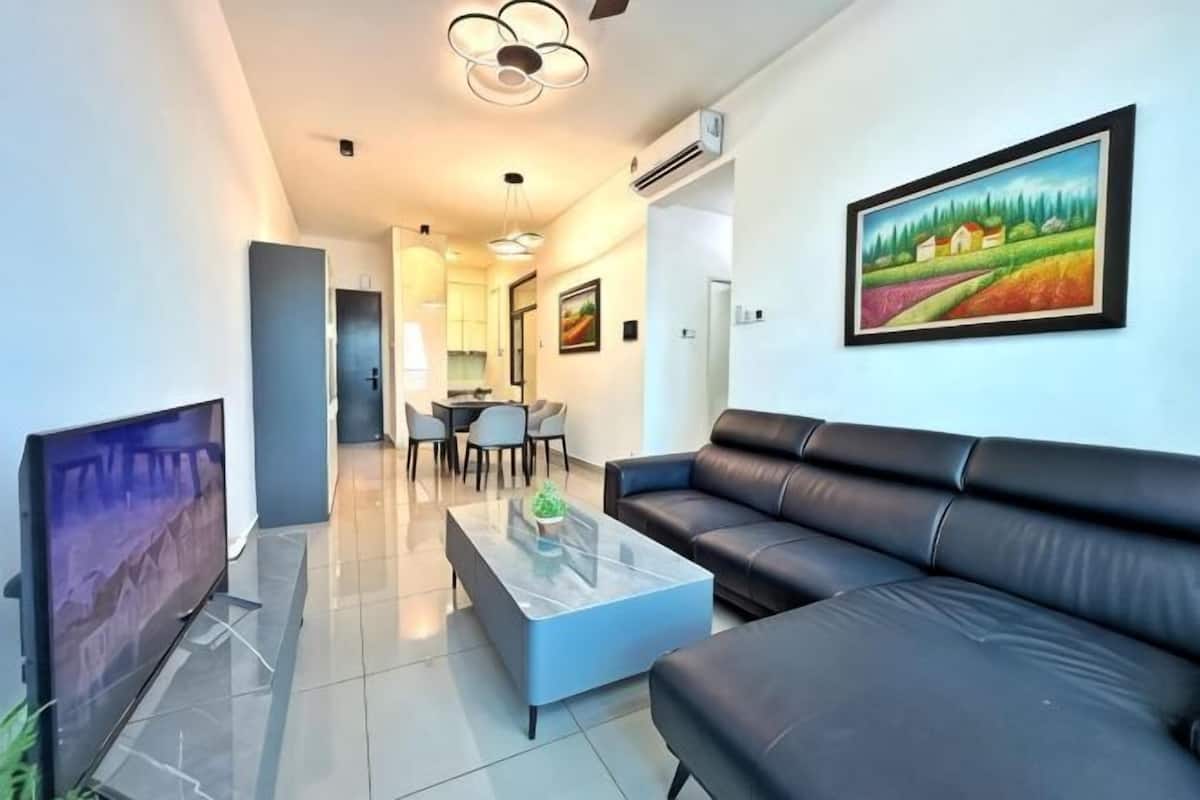 A modern living room with a flat-screen TV, a leather sofa, a glass coffee table, and a dining area with a table and chairs.