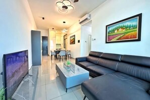 Uma sala de estar moderna com televisão de tela plana, sofá de couro, mesa de centro de vidro e um espaço de jantar com mesa e cadeiras.