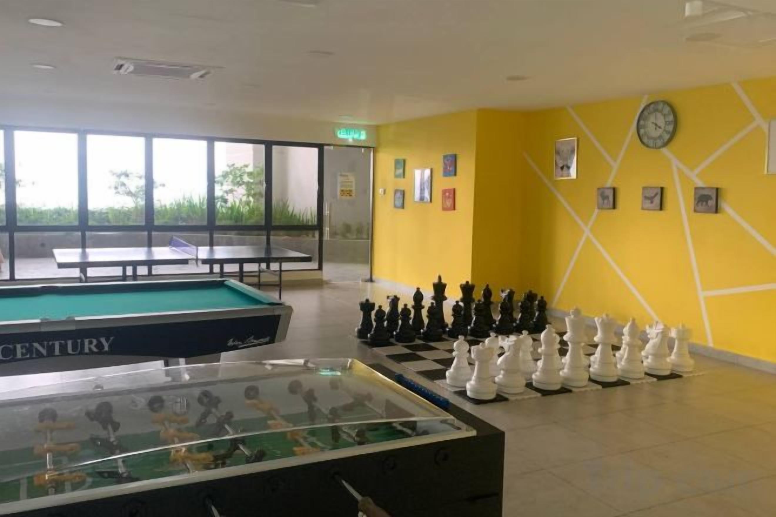 A pool table, a foosball table, and a chess set in a room with yellow walls and a clock.