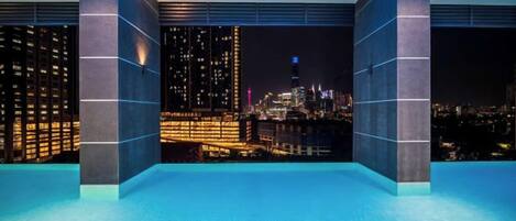 Ein modernes Hotelzimmer mit Blick auf die Stadt, großen Fenstern und einem geometrischen Deckenmuster.