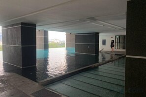 An indoor swimming pool with clear water, surrounded by dark pillars, and a person standing by the pool. - 2&3BR Family Suite Nr Sunway Velocity & LRT Maluri (Kuala Lumpur)