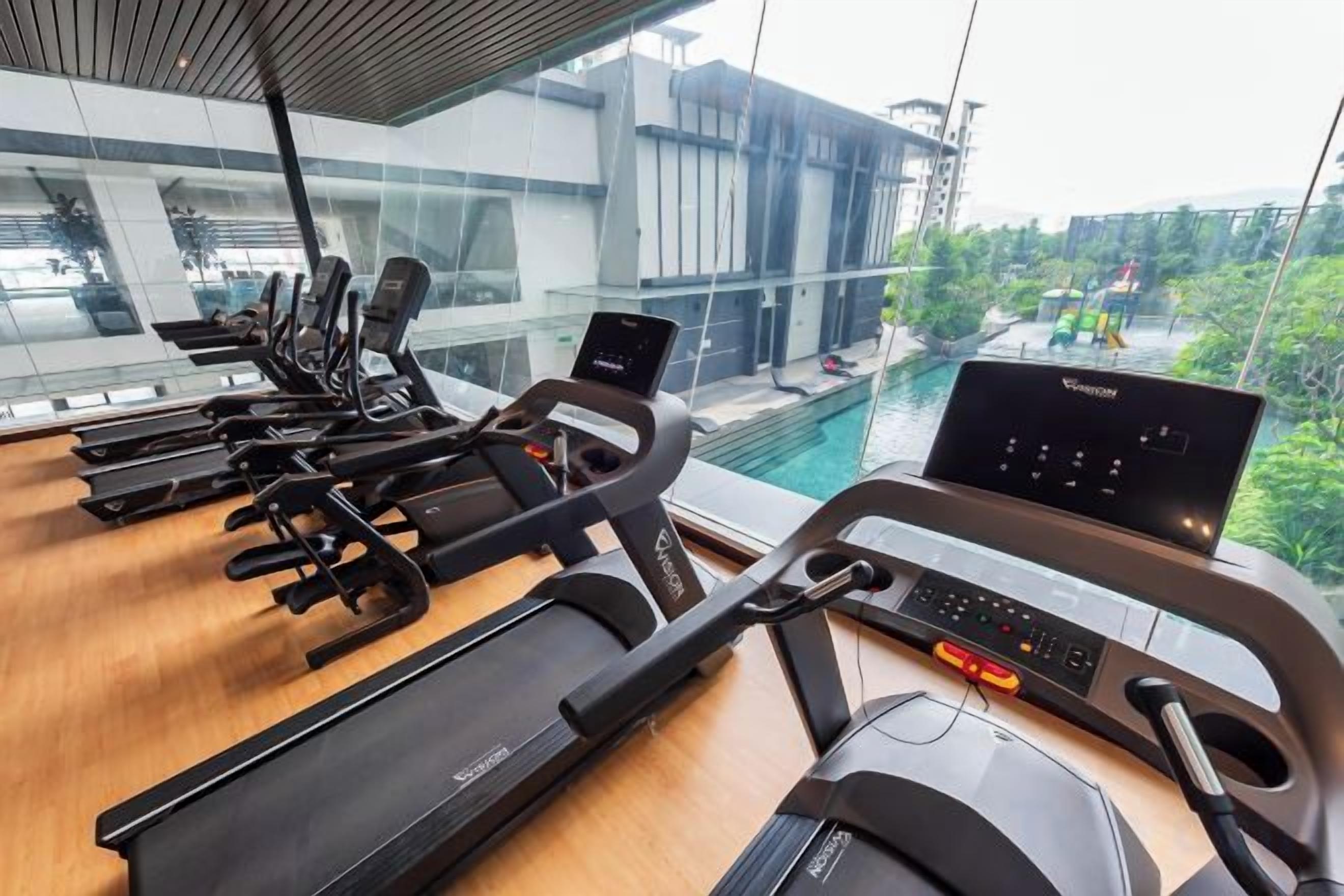 A gym with treadmills and a rowing machine, overlooking a swimming pool and greenery.