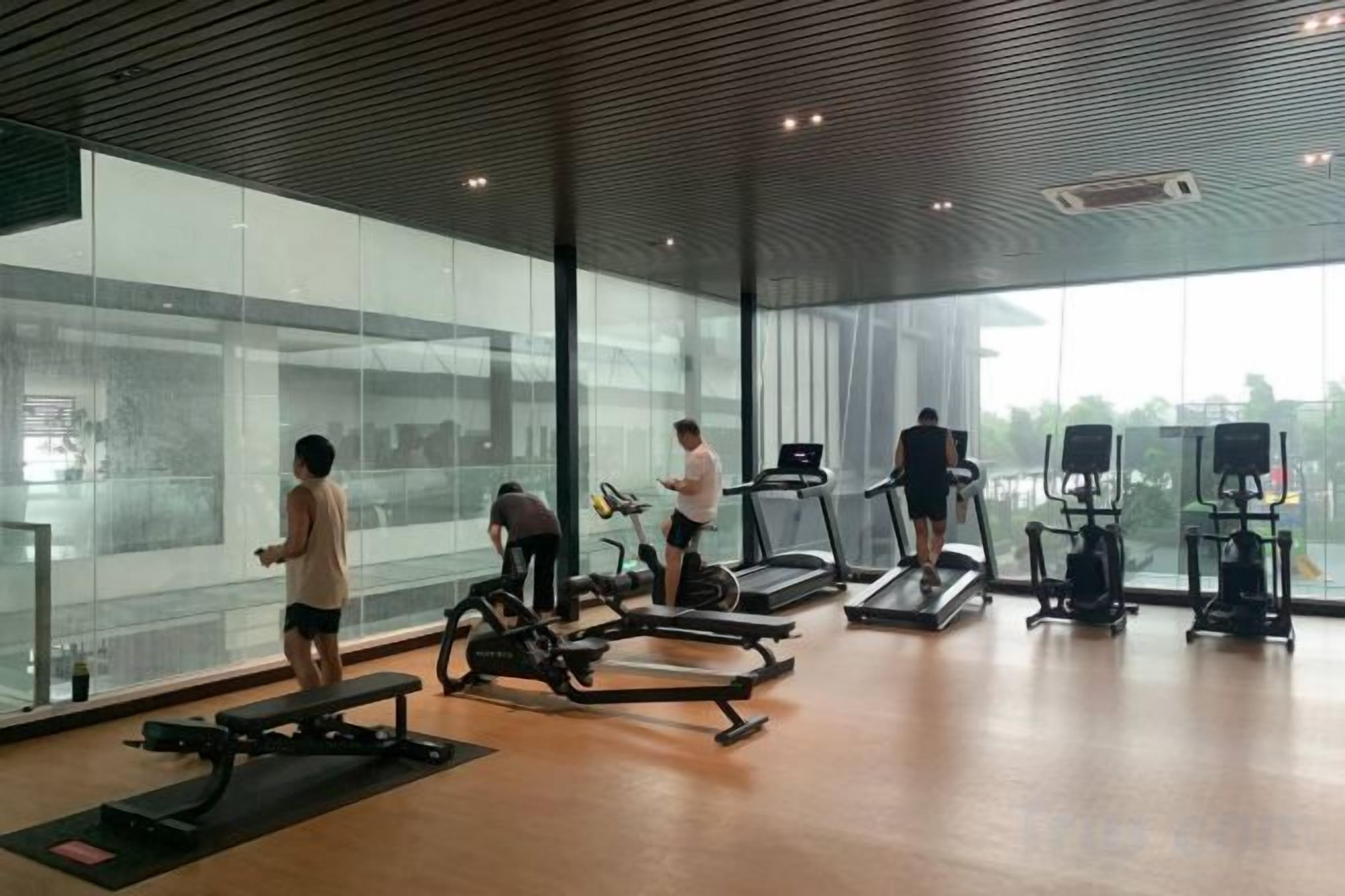 Ein Fitnessstudio mit Trainingsgeräten, großen Fenstern und Blick auf die Stadt.