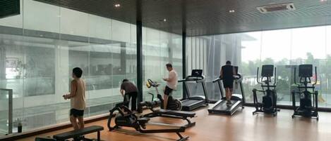 Ein Fitnessstudio mit Trainingsgeräten, großen Fenstern und Blick auf die Stadt.