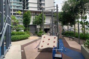 A playground with climbing structures and a blue play area, surrounded by greenery and residential buildings. - 2&3BR Family Suite Nr Sunway Velocity & LRT Maluri (Kuala Lumpur)