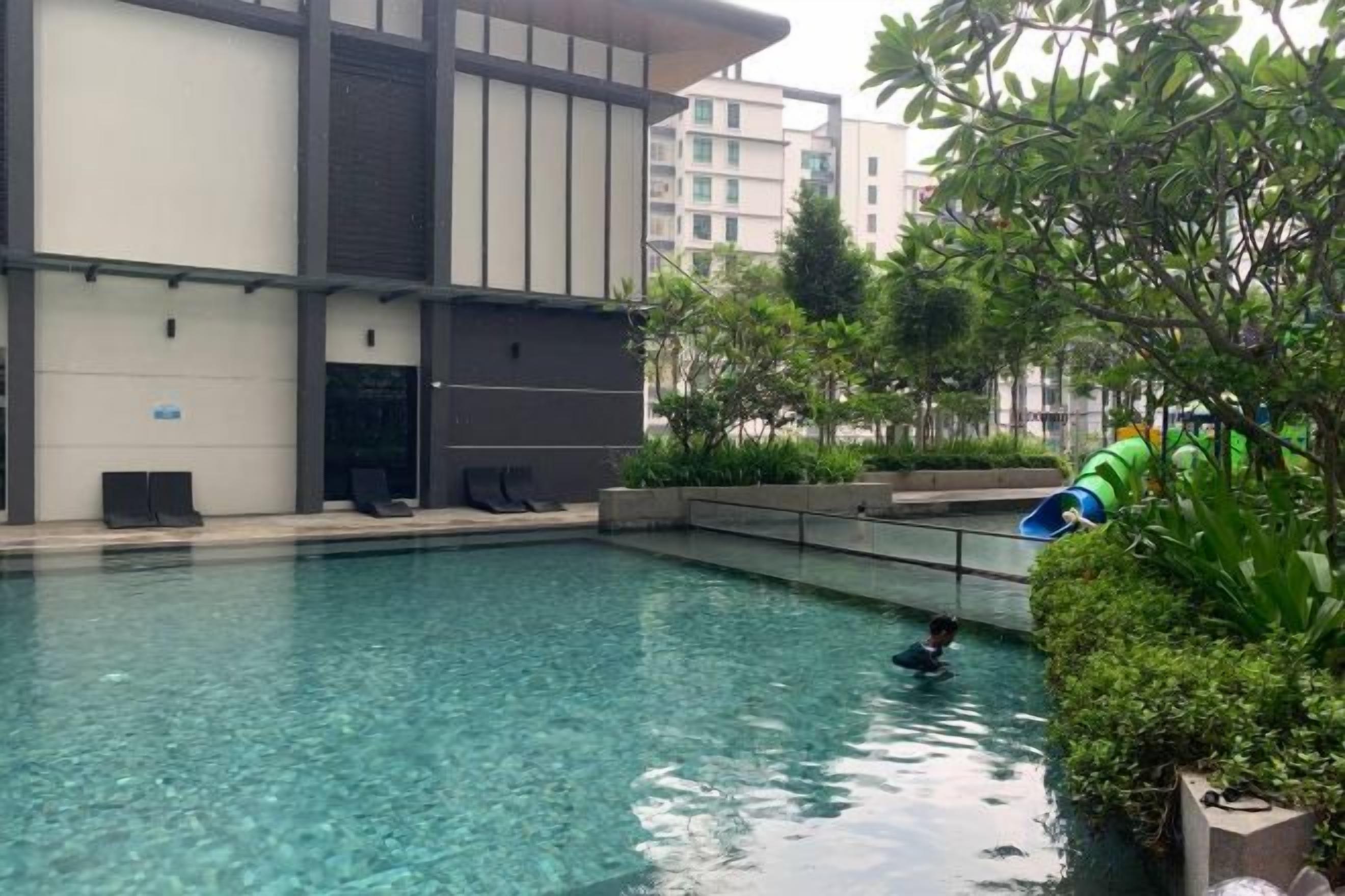A swimming pool with a person swimming, surrounded by greenery and a building with a modern design.