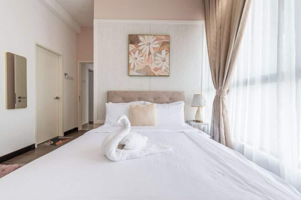 A hotel room with a large bed, a headboard, a painting on the wall, and a window with curtains.