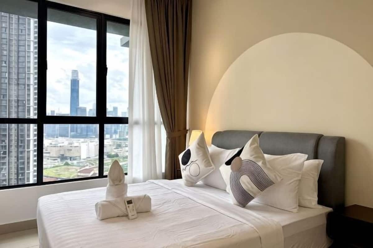 A hotel room with a large window, a neatly made bed, and a view of the cityscape.