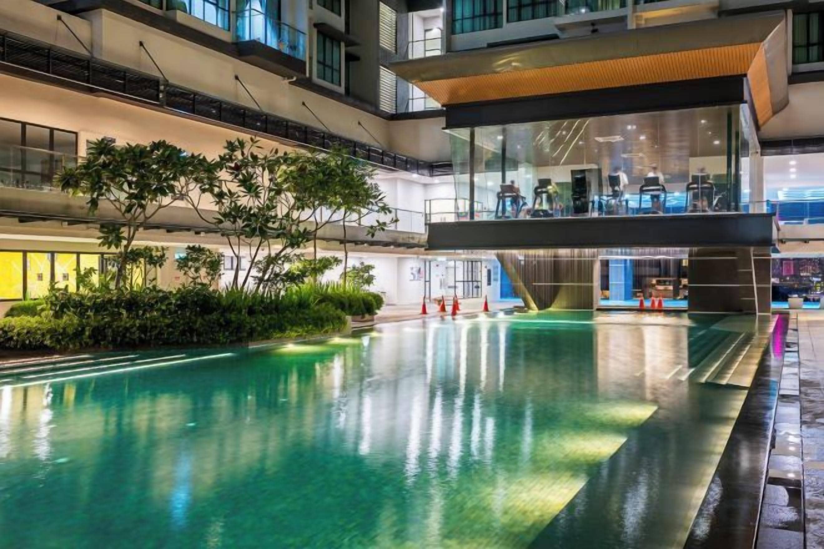 Una piscina interior con techo de cristal, rodeada de follaje y arquitectura moderna.