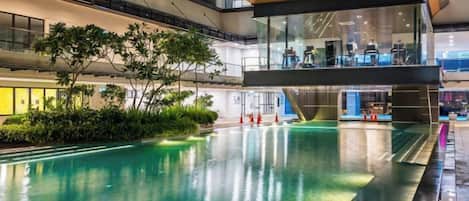 Una piscina interior con techo de cristal, rodeada de follaje y arquitectura moderna.