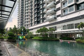 Um edifício moderno com piscina, rodeado por vegetação e uma área de recreação infantil.
