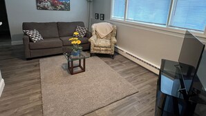 A living room with a brown sofa, a patterned armchair, a glass coffee table with yellow flowers, and a large window with blinds. - Nice 2-bedroom apartment in Anchorage (Anchorage)