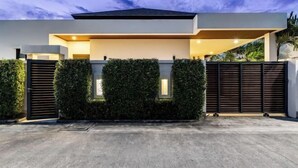 Une maison moderne avec un toit plat, une entrée sécurisée par un portail et une haie bien entretenue.