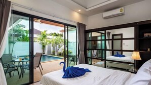 Une chambre d’hôtel avec un lit, une porte vitrée donnant sur un espace piscine, une petite table avec des chaises et une table de chevet avec une lampe.
