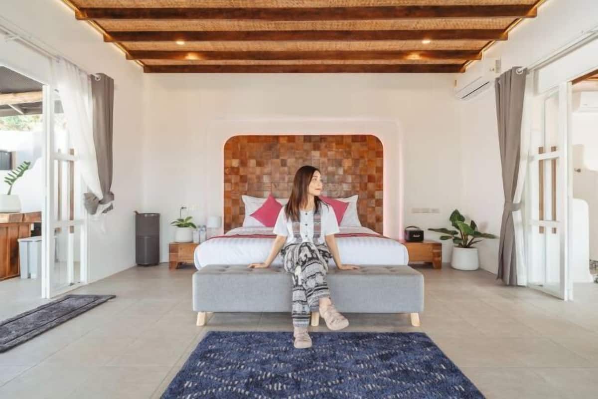 A modern bedroom with a large bed, a wooden ceiling, and a view of the outdoors.