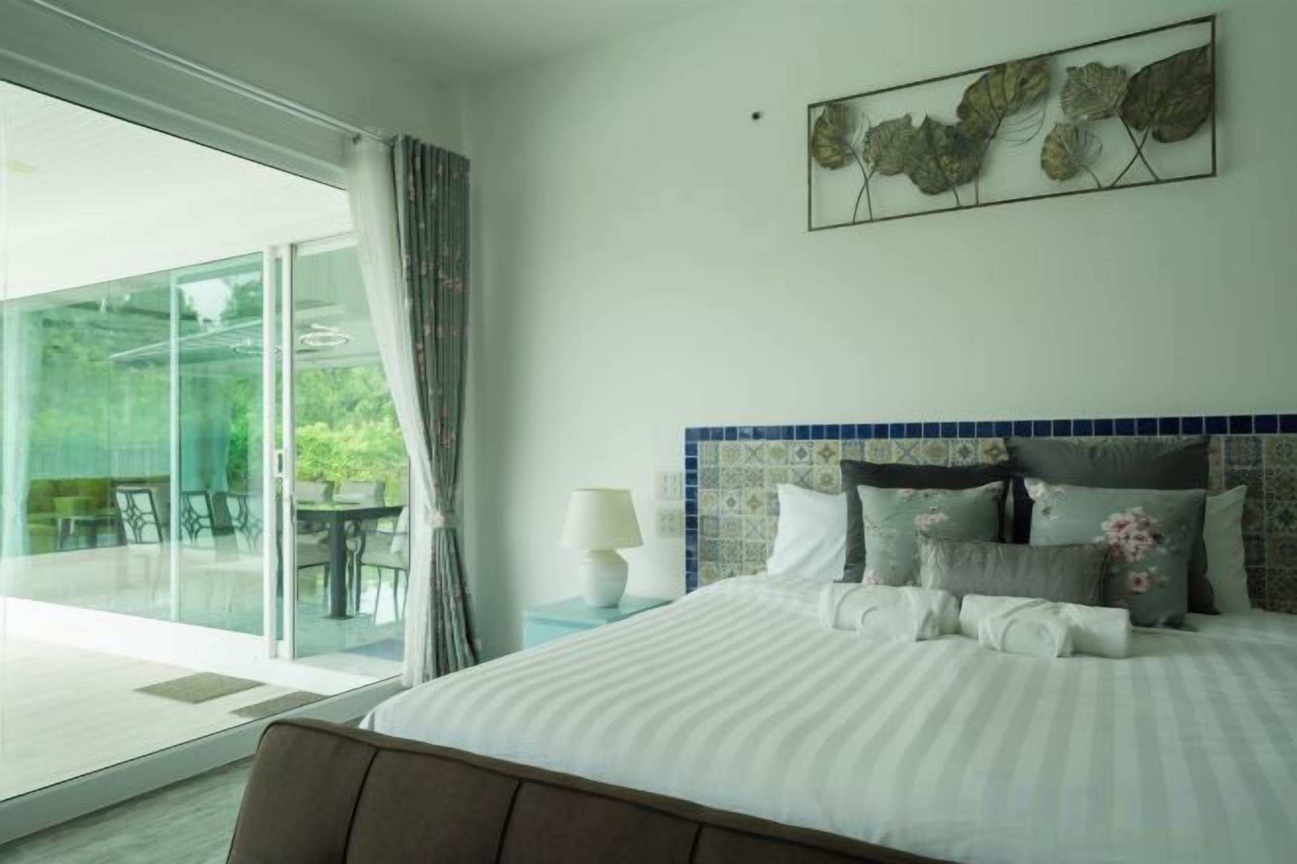 A bedroom with a bed, a nightstand, a lamp, and a view of a balcony.