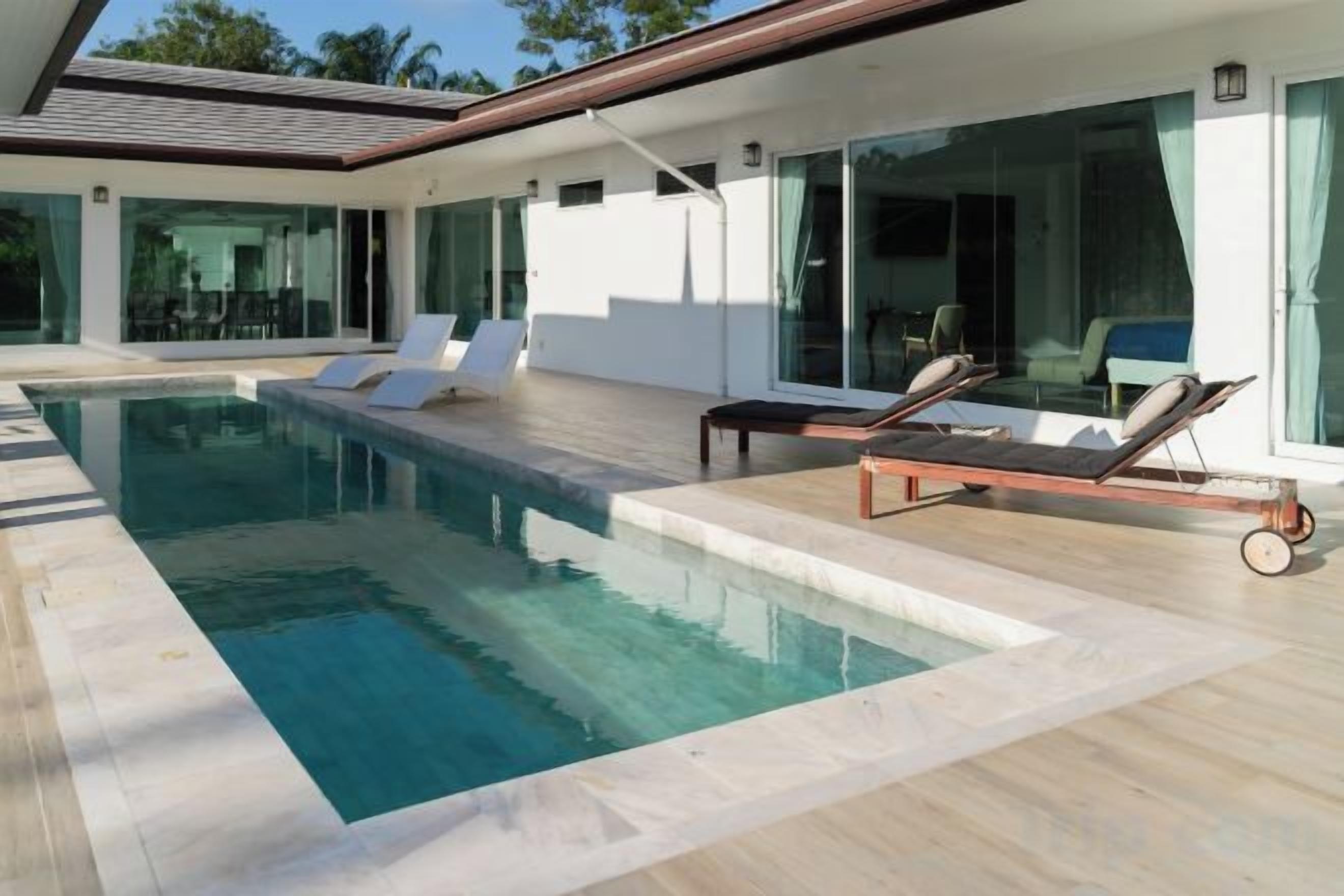 A modern pool area with lounge chairs, a clear pool, and a contemporary house design.