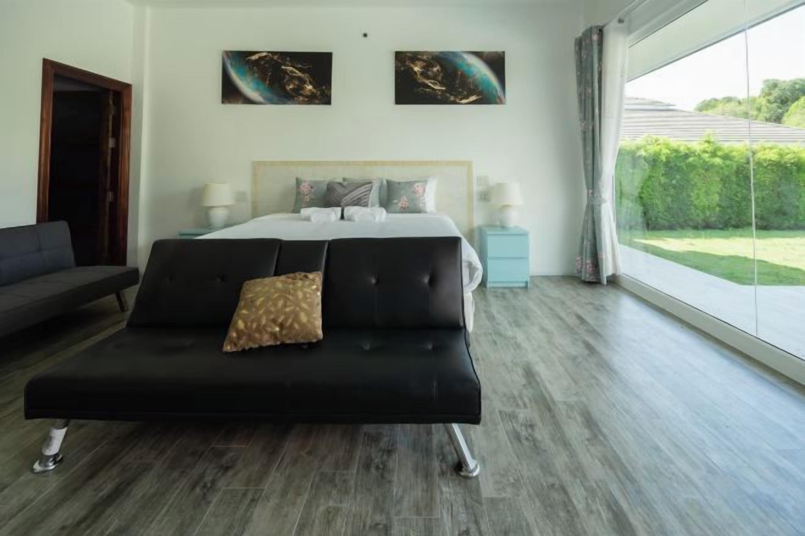 Un dormitorio moderno con una cama grande, un sofá negro y vistas a un jardín a través de un ventanal amplio.