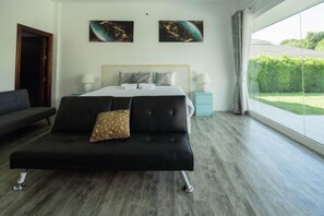 Un dormitorio moderno con una cama grande, un sofá negro y vistas a un jardín a través de un ventanal amplio.