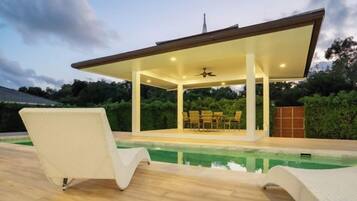 A covered outdoor area with a pool, lounge chairs, and a ceiling fan.