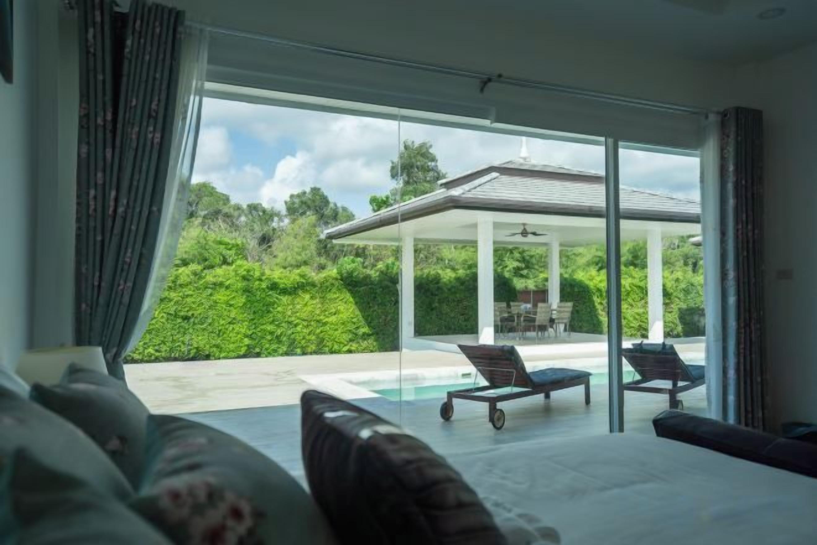 A modern interior with a large glass door leading to a pool area, a covered outdoor seating area, and a view of lush greenery.