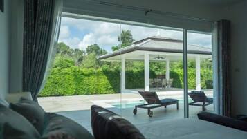 A modern interior with a large glass door leading to a pool area, a covered outdoor seating area, and a view of lush greenery.