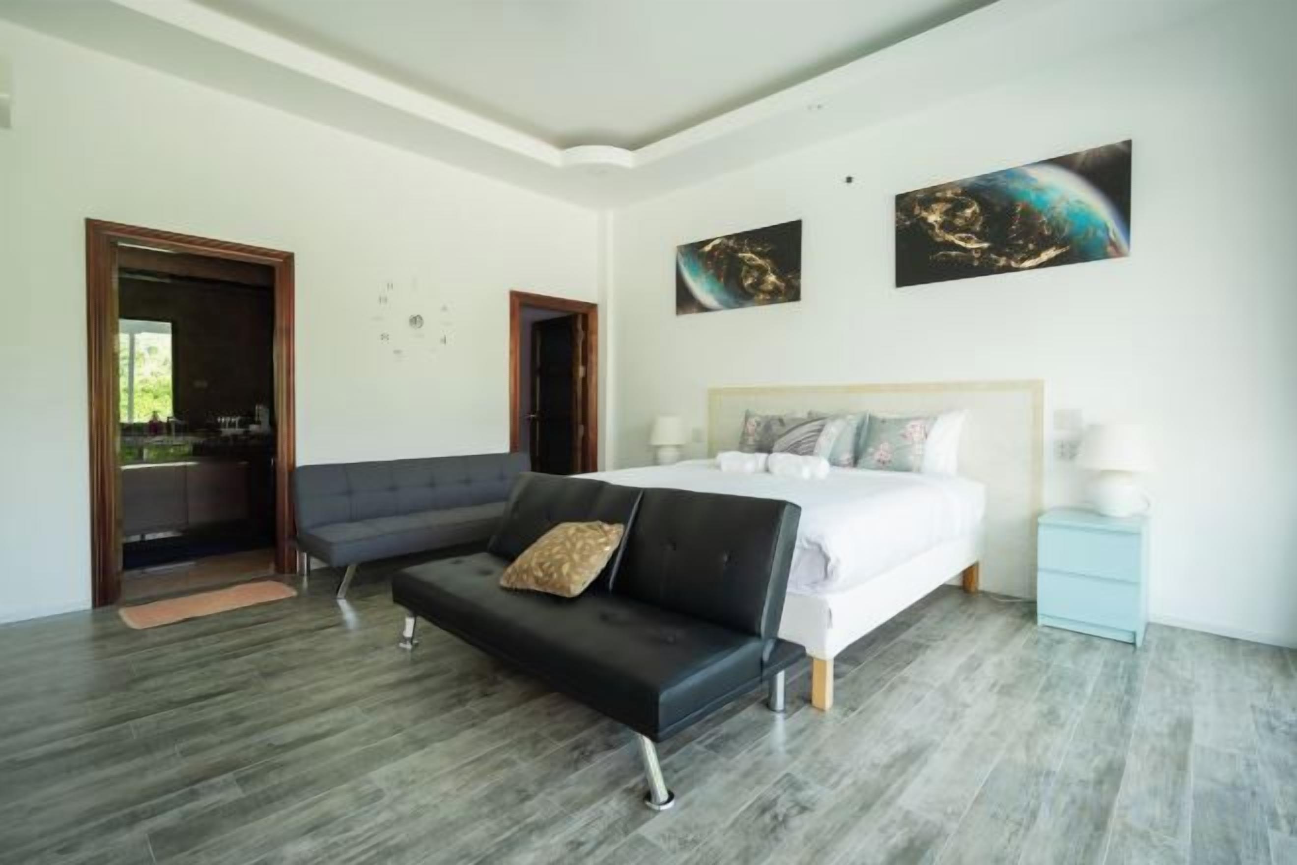 A bedroom with a bed, a sofa, a nightstand, and a door leading to a balcony.