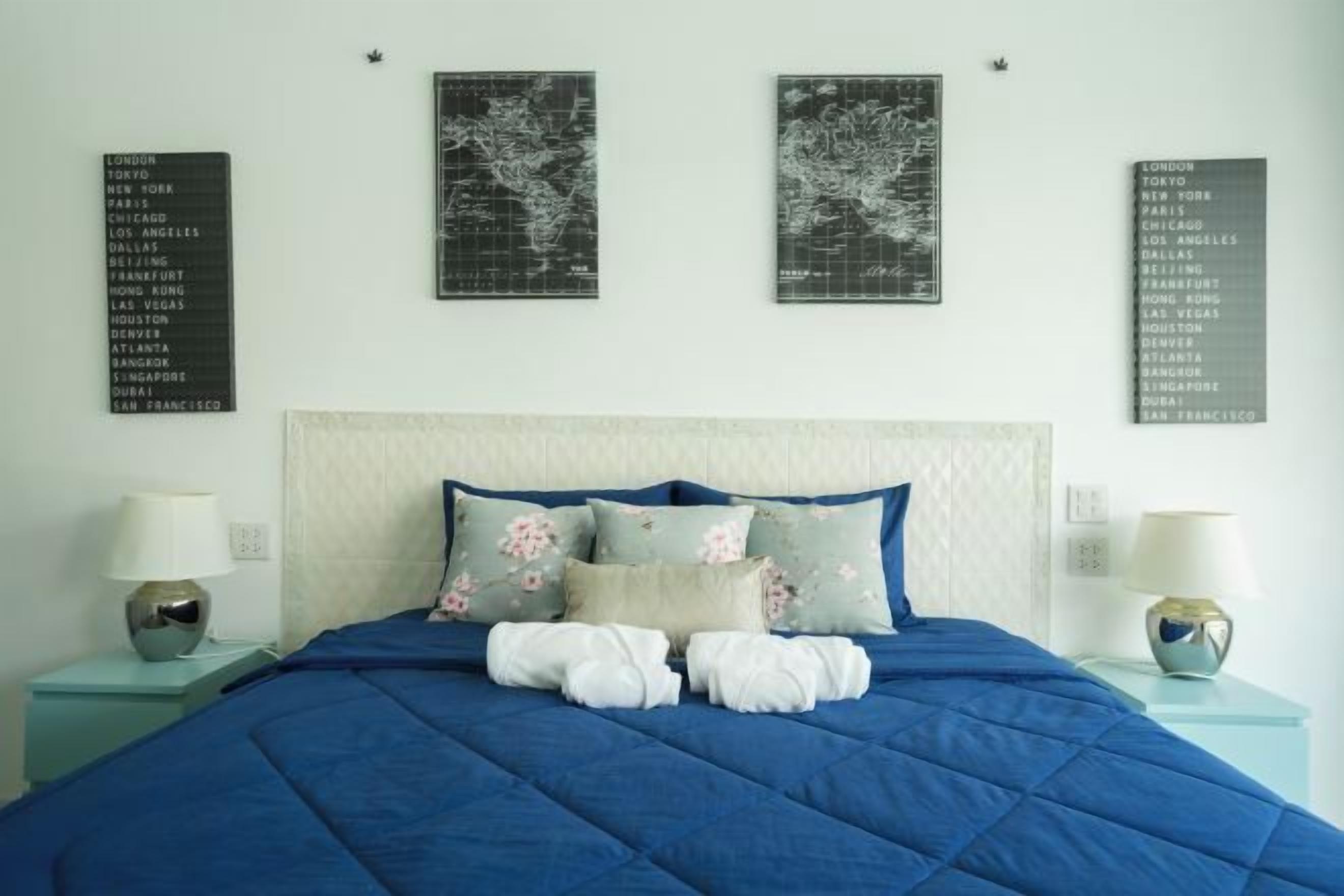 A bed with a blue quilt, pillows, and two bedside tables with lamps.