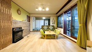 Ein Wohnzimmer mit Kamin, einer Couch, einem Esstisch und einem großen Fenster mit Vorhängen.