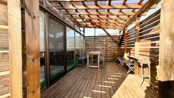 A wooden deck with a glass wall, tables, and a pergola.