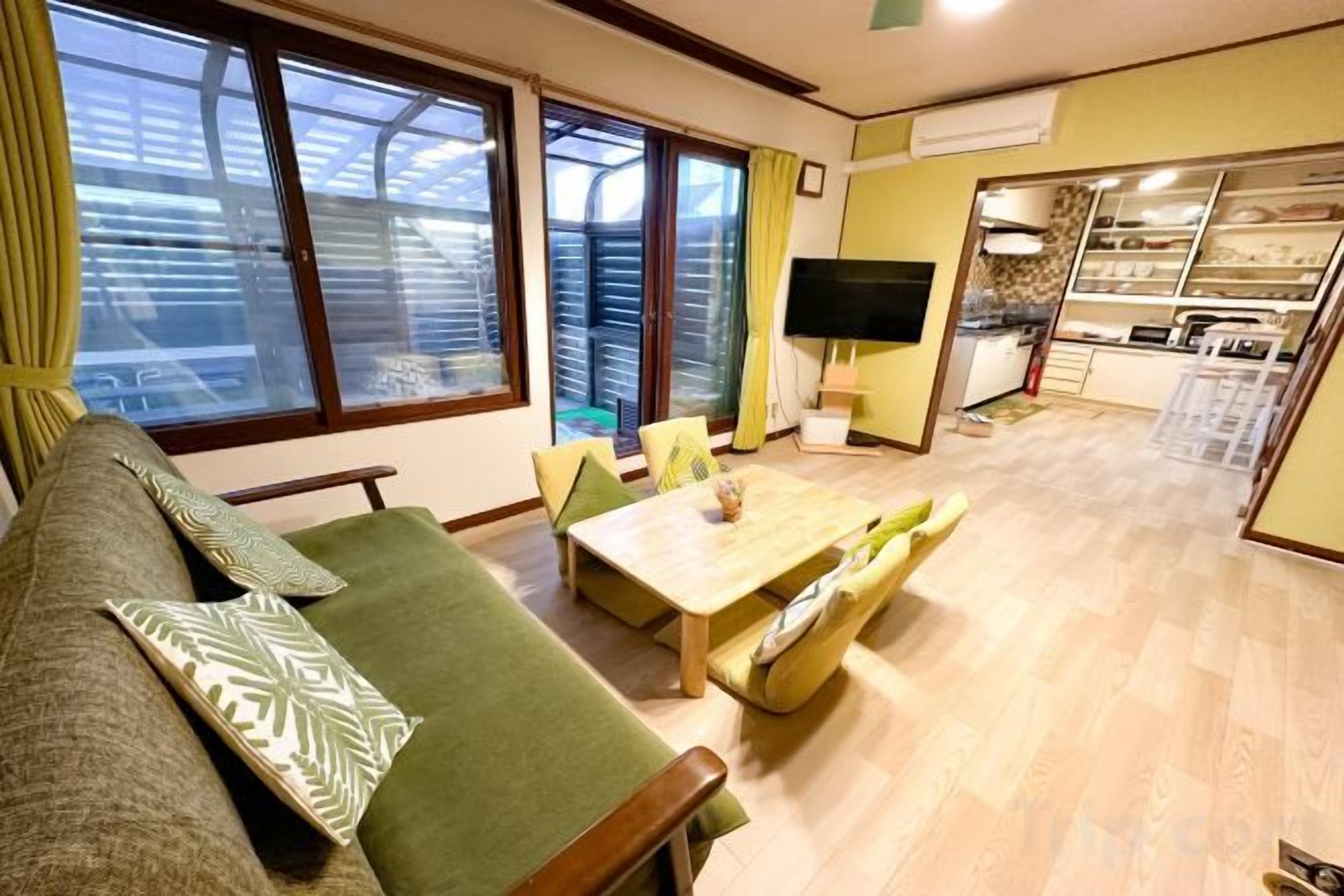 Sala de estar con sofá, mesa de comedor y televisor. Se observa un área de cocina al fondo.